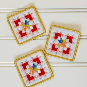 May include: Three square fabric patches featuring a white background with a central star pattern in red, light pink, yellow, and blue embroidery. Each patch is finished with a yellow stitched border, creating a uniform look for these textile items.