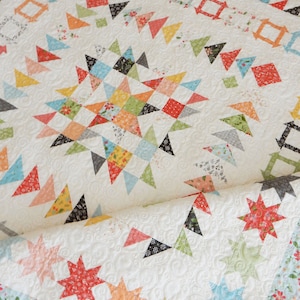 May include: A white quilt with a patchwork design featuring a variety of colors and patterns, including red, orange, yellow, green, blue, and black. The quilt is made up of squares, triangles, and stars. The quilt is folded in half and the edges are visible.