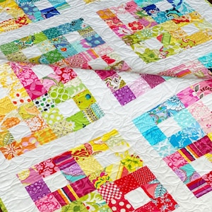 May include: A colorful patchwork quilt with a white background and a curved quilting pattern. The quilt is made of various fabrics with floral and geometric patterns in shades of pink, green, yellow, blue, and red.