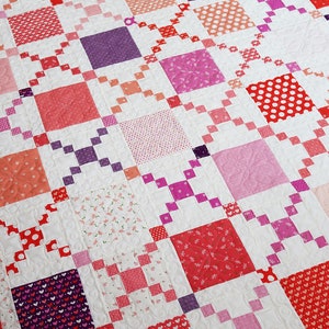 May include: A quilt with a patchwork design featuring various shades of pink, red, and white. The quilt is made up of squares with different patterns, including polka dots, hearts, and floral prints.