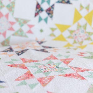 May include: A white quilt with a patchwork design featuring a variety of floral patterns in shades of pink, green, yellow, and blue. The quilt is made up of squares and triangles, creating a geometric pattern.