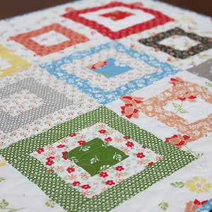 May include: A white quilt with a patchwork design featuring squares of different floral fabrics in shades of red, green, blue, yellow, and gray.