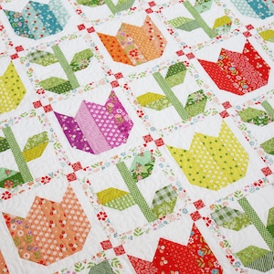 May include: A patchwork quilt with a white background and colorful tulip designs. The tulips are made from different fabrics and have a variety of patterns. The quilt is bordered with a floral print.