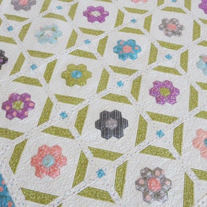 May include: A white quilt with a green and white geometric pattern. The quilt is made up of many small squares and rectangles, and it features a floral design in the center of each square. The quilt is quilted with a white thread, and it has a white border.