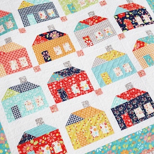 May include: A handmade quilt featuring a repeating pattern of colorful houses. Each house is a unique patchwork design with various patterns and colors, including red, blue, yellow, and green. The quilt is bordered with a floral pattern.