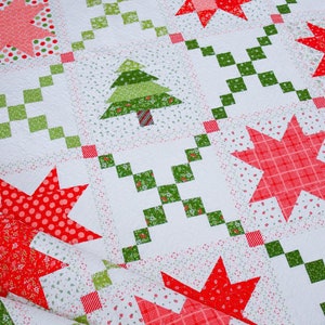 Könnte beinhalten: Eine weiße Steppdecke mit Weihnachtsmotiv. Die Steppdecke zeigt rote und grüne Sterne, Bäume und karierte Muster. Die Steppdecke ist zur Hälfte gefaltet und liegt auf einem Holzboden.