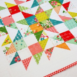 May include: A colorful patchwork quilt with a red and white gingham border. The quilt is made up of squares and triangles in various shades of pink, red, green, yellow, and blue. The quilt is quilted with a simple straight stitch.