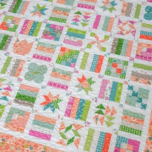May include: A patchwork quilt featuring a grid of square blocks with varied patterns in shades of green, pink, orange, and white. The blocks include star, pinwheel, and floral motifs, all framed by a wide border with a white and orange floral print.