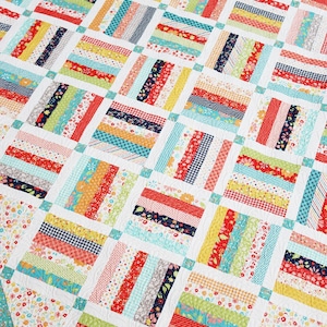 May include: A colorful patchwork quilt with a white background. The quilt features rectangular blocks with strips of various patterned fabrics in red, yellow, blue, and green. The border has a floral pattern.