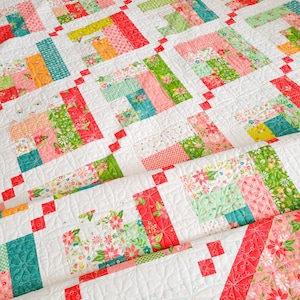 Puede incluir: Una colcha con un diseño de patchwork que presenta una variedad de estampados florales en tonos de rosa, verde, amarillo y azul. La colcha está acolchada con hilo blanco y tiene un borde rojo.