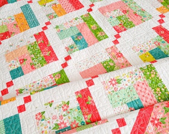 May include: A quilt with a patchwork design featuring a variety of floral prints in shades of pink, green, yellow, and blue. The quilt is quilted with a white thread and has a red border.