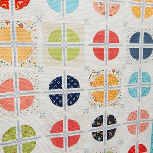May include: A quilt with a white background and a pattern of colorful circles with a cross design inside each circle. The circles are arranged in a grid pattern.