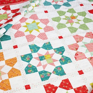 May include: A white quilt with a patchwork design featuring a variety of floral and geometric patterns in shades of red, green, yellow, and blue.