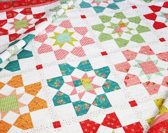 Puede incluir: Una colcha blanca con un diseño de patchwork que presenta una variedad de patrones florales y geométricos en tonos de rojo, verde, amarillo y azul.
