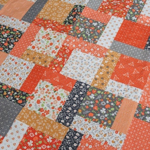 May include: A patchwork quilt with a variety of floral and geometric patterns in shades of orange, white, gray, gold, and black. The quilt is made of rectangular and square fabric pieces sewn together in a staggered design.