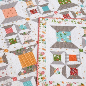 May include: A quilt with a white background and a pattern of squares in various colors and patterns, including orange, green, blue, and red. The quilt is bordered with a floral print fabric.