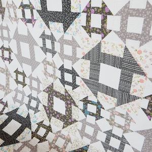 May include: A quilt made of various fabrics in shades of gray, black, and white with floral patterns. The quilt is made up of squares and triangles, creating a geometric design.
