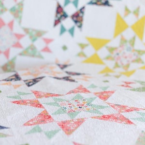 May include: A white quilt with a patchwork design featuring a variety of floral patterns in shades of pink, green, yellow, and blue. The quilt is made up of squares and triangles, creating a geometric pattern.