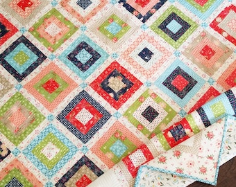May include: A quilt with a diamond pattern in shades of pink, red, blue, green, and white. The quilt is made of fabric with floral prints and polka dots.