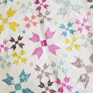 May include: A white quilt with a patchwork design featuring various floral patterns in shades of pink, yellow, teal, and brown. The quilt is quilted with a swirling pattern.