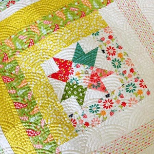 May include: Close-up of a colorful quilt with a star design. The quilt features a white background with quilted patterns, and is accented with yellow, green, and floral patterned fabrics. The star is made of red, green, and floral fabrics.