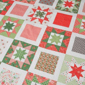 May include: A patchwork quilt featuring a repeating pattern of squares and star shapes. The quilt uses a palette of red, green, pink, and gray fabrics on a white background. The star blocks are surrounded by green and red floral patterns.