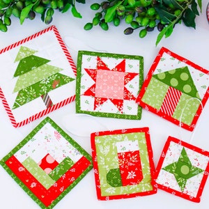 Pode incluir: Seis enfeites de Natal acolchoados feitos à mão em uma variedade de designs natalinos, incluindo uma árvore, uma estrela, uma meia e uma casa. Os enfeites são feitos de tecido vermelho, verde e branco e têm um fundo branco.