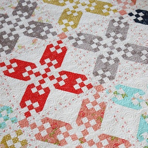 May include: A quilt with a patchwork design featuring a variety of colors and patterns, including red, white, blue, yellow, and pink. The quilt is made up of squares and diamonds, and the fabric is quilted with a swirling pattern.