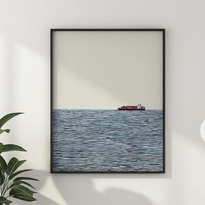 以下が含まれることがあります： ミニマリストな海の風景を描いた、額装されたアートプリント。赤と白の貨物船が、水平線のある青い海に浮かび、薄いベージュ色の空を背景にしています。黒いフレームがモダンな美しさを引き立てています。