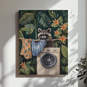 May include: A whimsical art print featuring a raccoon holding laundry above a washing machine. The raccoon is surrounded by lush green foliage and orange flowers. Clothes are hanging on a line. The artwork has a tropical theme.