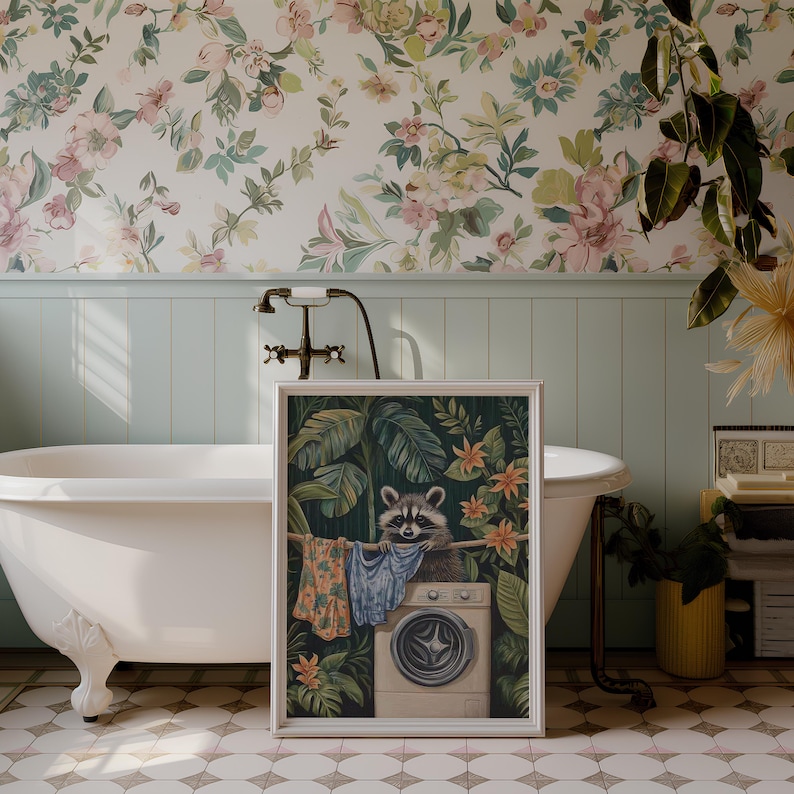 May include: A framed art print featuring a raccoon perched on a washing machine, with laundry hanging on a clothesline. The artwork is set against a backdrop of lush green foliage and orange flowers. The frame is white, and the overall theme is whimsical and nature-inspired.