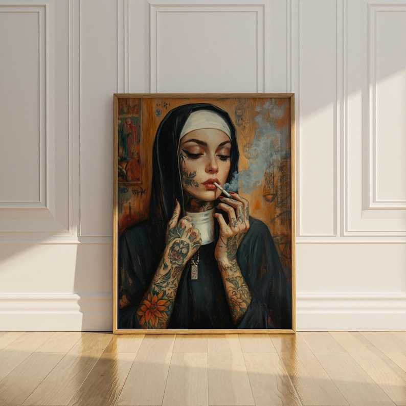 May include: Framed artwork featuring a nun with tattoos smoking a cigarette. The nun is wearing a black habit and white wimple. Her arms and face are covered in tattoos. The artwork has a gold frame and is displayed against a white wall.