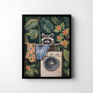 May include: A framed art print depicts a raccoon hanging laundry on a clothesline. The raccoon is perched above a washing machine, surrounded by lush green foliage and orange flowers. The clothesline holds colorful garments.