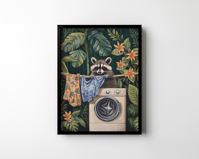 May include: A framed art print depicts a raccoon hanging laundry on a clothesline. The raccoon is perched above a washing machine, surrounded by lush green foliage and orange flowers. The clothesline holds colorful garments.