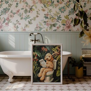 Peut inclure: Une impression encadr&eacute;e d'un chien assis sur des toilettes et lisant un journal dans un d&eacute;cor de jungle. L'impression est accroch&eacute;e dans une salle de bain avec une baignoire &agrave; pieds blancs et un papier peint fleuri.