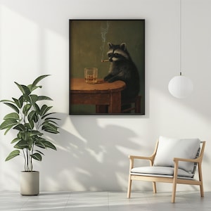 May include: A framed art print depicts a raccoon seated at a small wooden table, smoking a cigarette and with a glass of amber liquid. The raccoon is dark gray and black, with a white face. The background is a muted green.