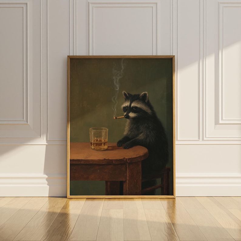 May include: A framed art print depicts a raccoon seated at a small wooden table, smoking a cigarette. A glass of amber liquid sits on the table. The raccoon is rendered in dark tones against a green background.