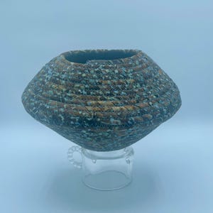 May include: A woven bowl with a brown and blue pattern. The bowl is made of fabric and has a unique, rounded shape.