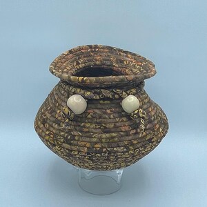 May include: A small, brown woven basket with a round base and a wide opening. The basket is decorated with white beads around the rim.