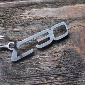 Puede incluir: Un llavero de metal plateado con un anillo de llave y el número "30" cortado en el metal.