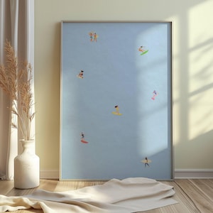 May include: A framed art print featuring a light blue background with several small figures surfing. The figures are depicted in various colors, riding surfboards. The artwork is displayed in a silver frame, creating a minimalist aesthetic.