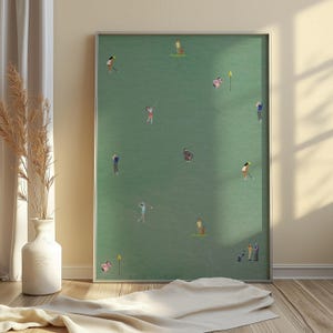 Puede incluir: Una impresión enmarcada verde y blanca de un campo de golf con varias personas jugando al golf. La impresión está en un marco plateado y está colgada en una pared.