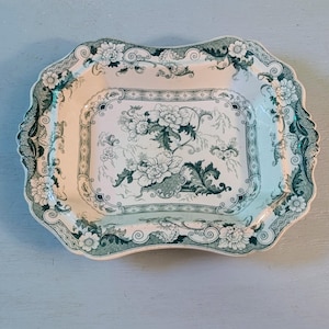 May include: A white ceramic mug with a black handle and the text "But First, Coffee" in a bold, black font. The mug is set against a blurred background, highlighting its clean design.