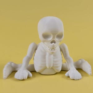 May include: A matte white 3D printed figurine of a skeleton torso with a skull, rib cage, and arms. The skeleton is depicted in a seated position with legs extended outward to the sides, featuring visible joints and a smooth, monochromatic surface.