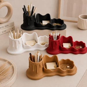 May include: Four desk organizers in black, white, red, and tan. Each features a cylindrical pen holder with a vertical ribbed texture and a dripping wax design, connected to two rounded, scalloped-edge trays for holding small office supplies.