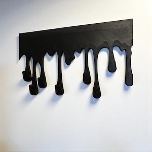 May include: A black wall-mounted coat rack featuring a horizontal top bar with multiple vertical extensions that mimic the appearance of dripping liquid. The design includes several integrated hooks at the ends of the drips for hanging items.