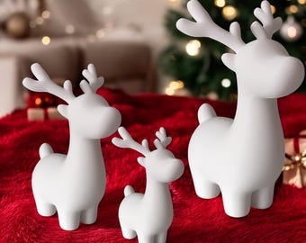 May include: Three matte white reindeer figurines of varying sizes standing upright. Each deer features a smooth, rounded body, a short tail, and branched antlers. The figures are arranged in a group, displaying a consistent solid white color.