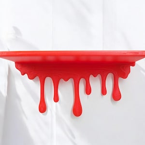Könnte beinhalten: Ein leuchtend rotes Wandregal mit einer flachen Oberseite und einer dekorativen Unterkante, die wie flüssige Farbe gestaltet ist, welche in verschiedenen Längen und Breiten nach unten tropft und einen markanten visuellen Effekt erzeugt.