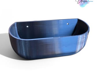 May include: A semi-oval, wall-mounted storage bin with a smooth, dark blue finish. The container features a flat back panel with two small, circular mounting holes near the top edge and a deep, open-top basin for holding various small items.