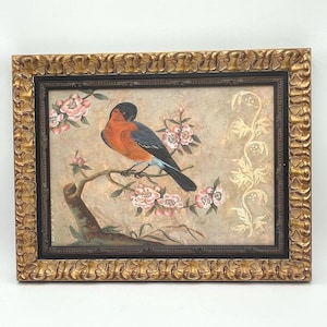 Può includere: Un dipinto incorniciato di un uccello posato su un ramo con fiori rosa. L'uccello ha un corpo blu e arancione ed è posto su uno sfondo crema con accenti dorati.